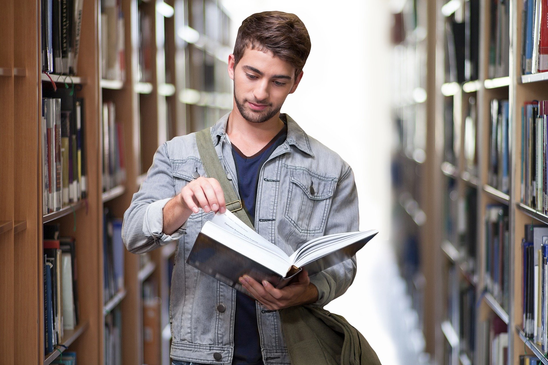 A young man in a denim jacket holds an open book in his hand.