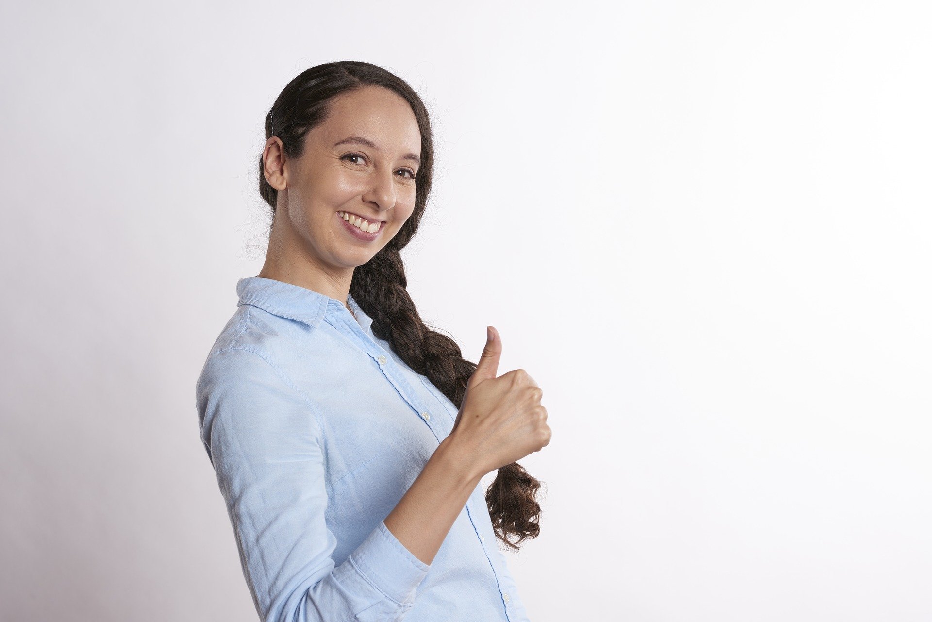 A smiling girl in a blue blouse raises her thumb up.